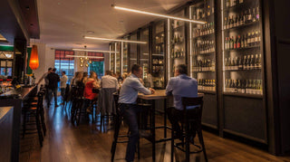 Bar interior with people and shelves of wine bottles.