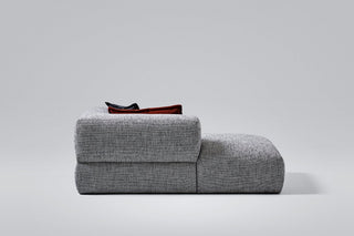 Gray upholstered ottoman with a dark object on top.