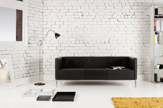 Black leather sofa against white brick wall