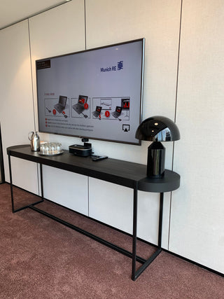 TV display with Munich RE, black console table, and lamp.