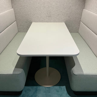Modern booth with a white table and gray cushioned benches against a textured wall.