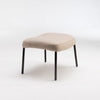 Beige upholstered stool with black legs.