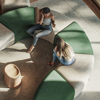 Two women sitting on a curved green and beige sofa.