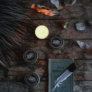 Candle, tins, book, and feather on wood.
